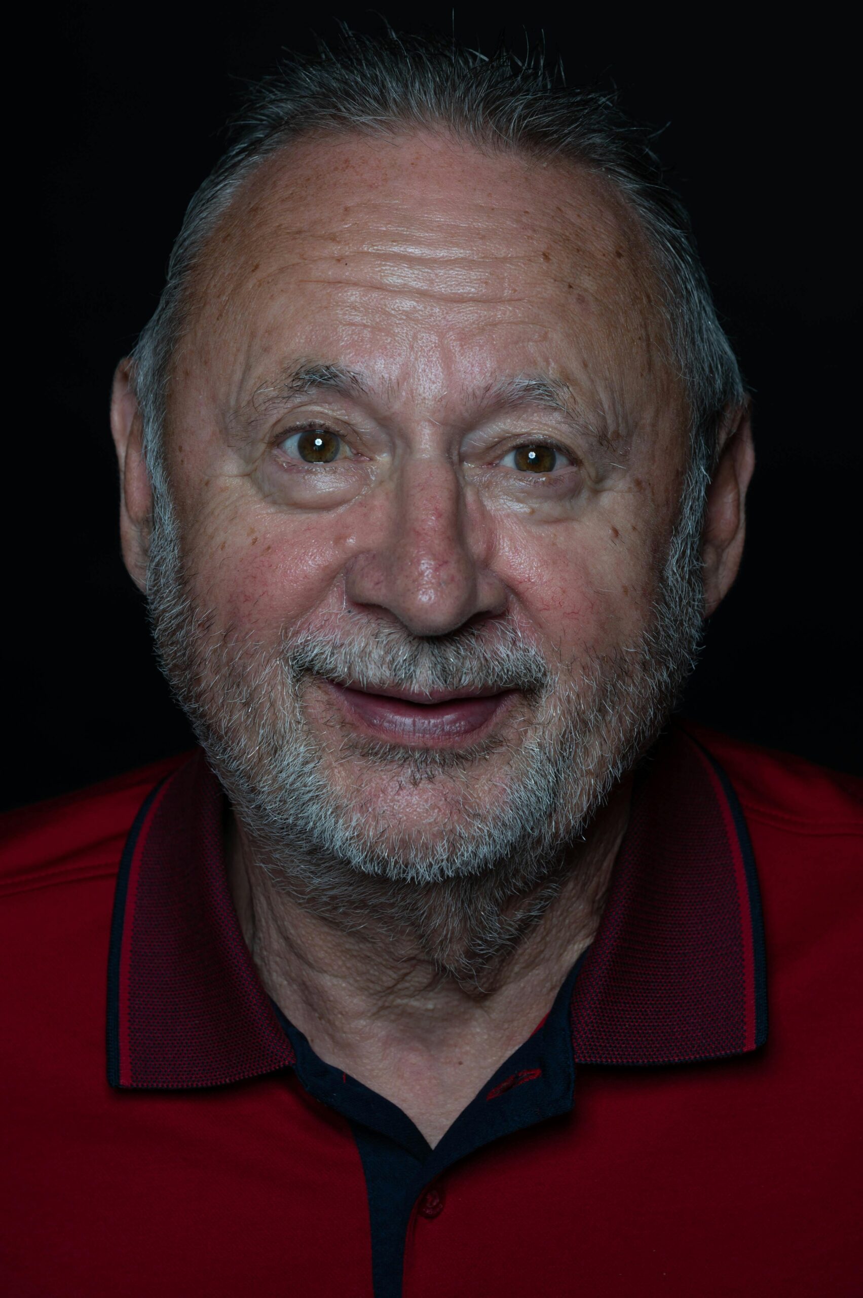 Close-up portrait of a smiling senior man with a beard wearing a red shirt.